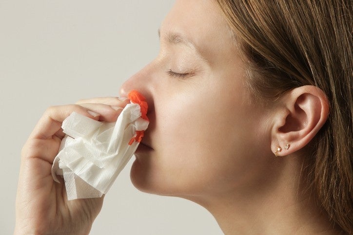 A woman blowing her nose with a tissue, likely addressing a nosebleed issue.